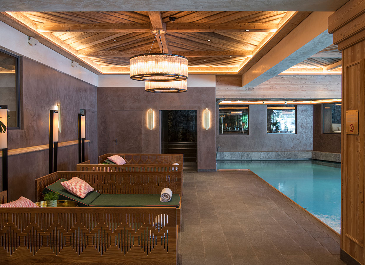 Luxuriöser Spa-Bereich mit Indoor-Pool, stilvollen Liegeflächen und stimmungsvoller Beleuchtung in einem Chalet mit Holz- und Steinelementen.