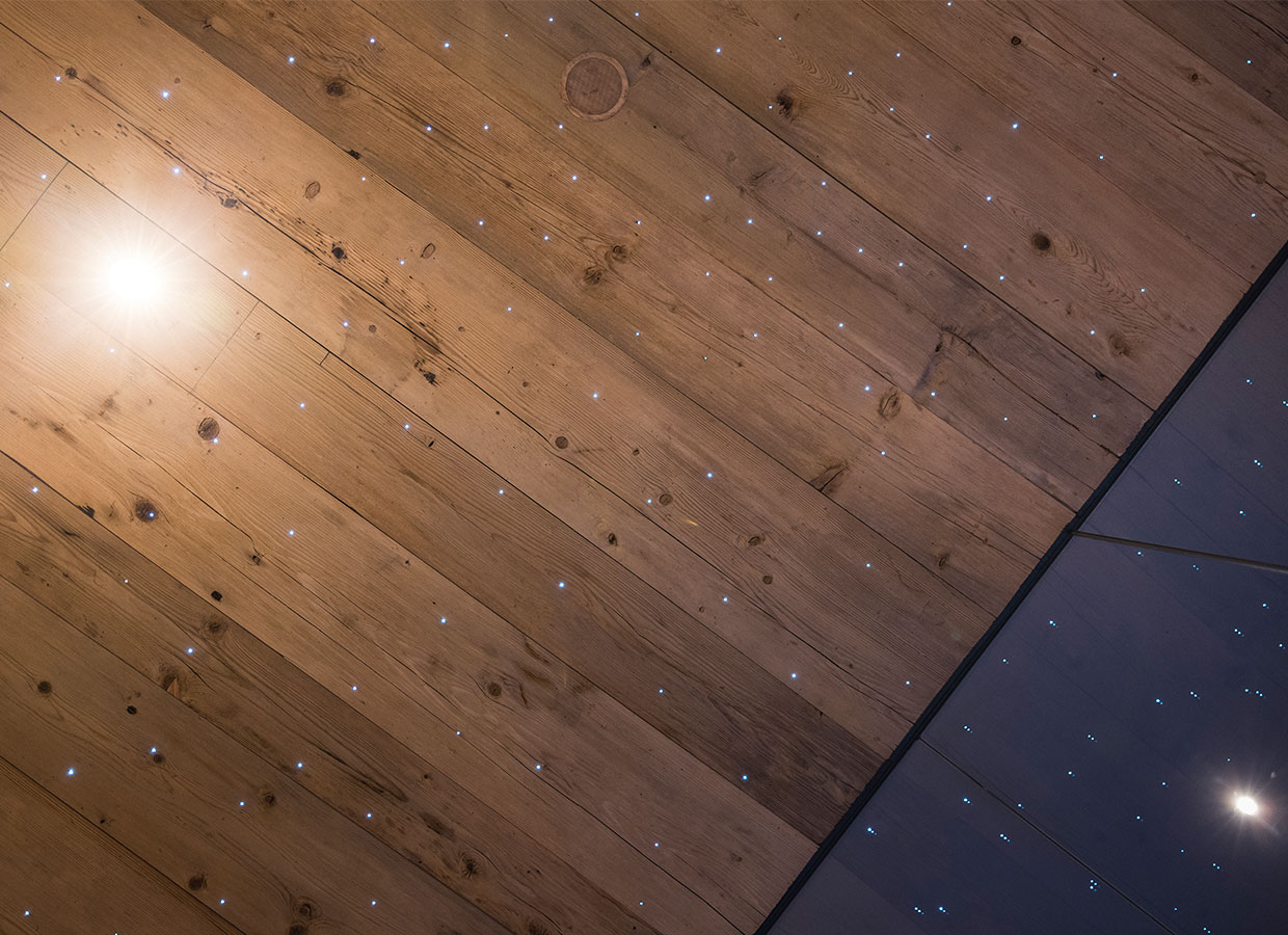 Detailaufnahme einer Holzdecke mit integrierten LED-Lichtpunkten, die einen Sternenhimmel simulieren.